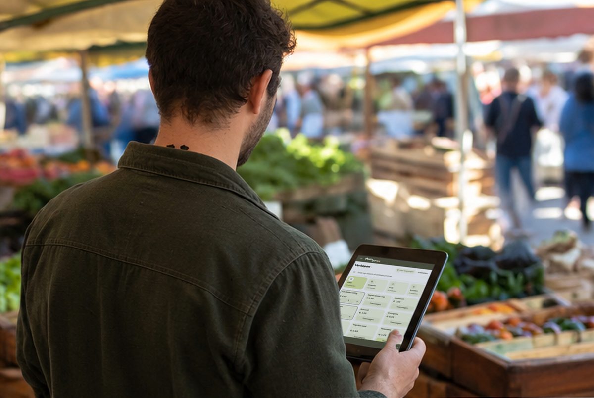 Een marktkoopman met een tablet in de hand. Op het scherm staat de verkooppagina van MarktAmigo met groente en fruit.